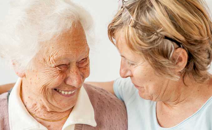 A woman gives a side hug to her elderly mother