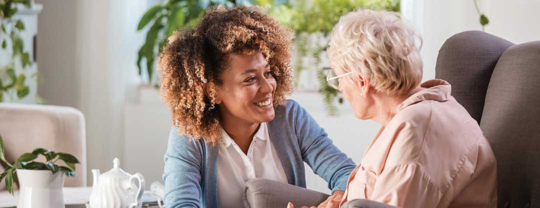 A woman visits an elderly woman sitting in an armchair