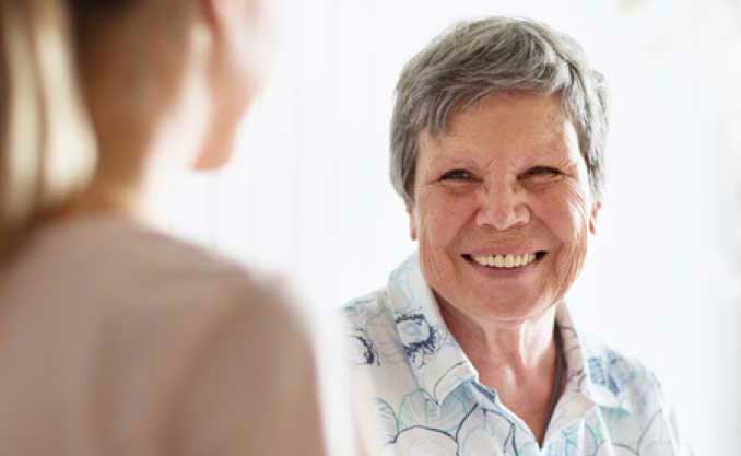 An elderly woman smiles at a woman