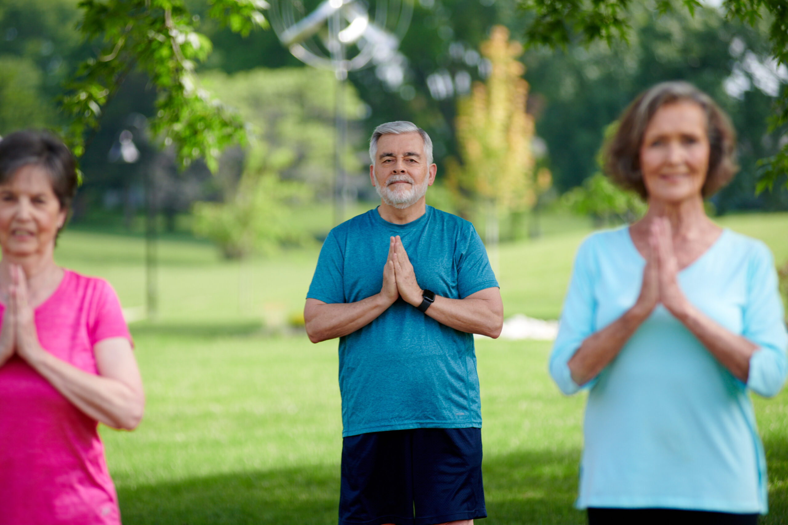 three seniors doing yoga outside on grass