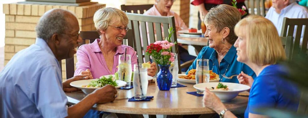 Four older adults saving a chef-prepared meal together in the dining room, sharing laughter and companionship in the heart of John Knox Village.