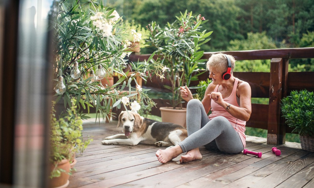 Happy senior woman listening to music on a porch with her dog