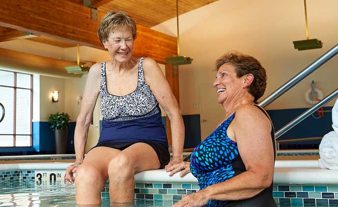 Two women by the pool's edge wearing swimsuits