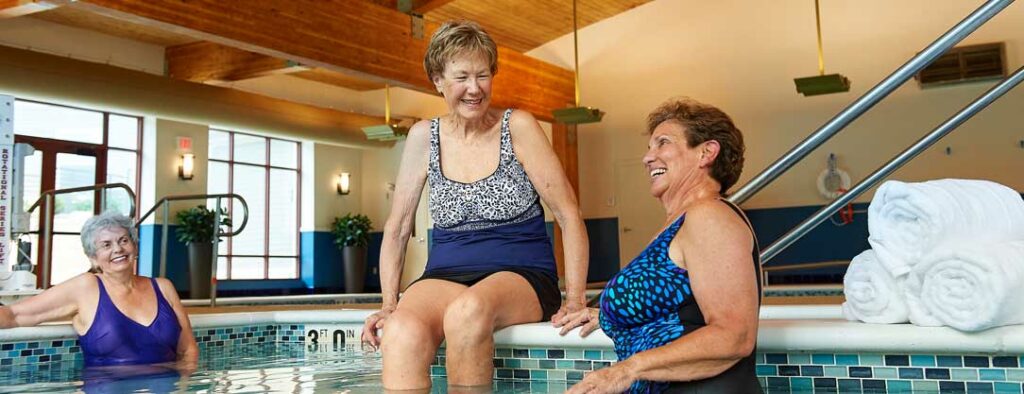 Three senior women enjoying a refreshing swim in a community pool, showcasing active and vibrant retirement living at John Knox Village.