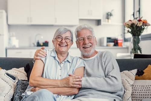Happy,Mature,Husband,And,Wife,Sit,Rest,On,Couch,At Two seniors smiling on their couch
